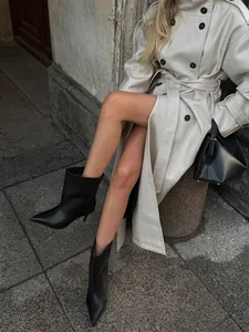 Close-up of a women's cream double-breasted trench coat styled with black ankle boots