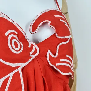 Detailed view of intricate white goldfish embroidery on a red sleeveless summer dress