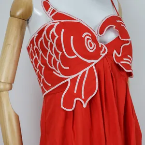 Macro detail view of vibrant red dress featuring exquisite white goldfish embroidery