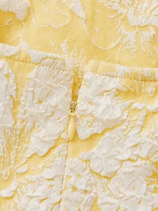 Close-up detail of yellow dress with white 3D floral textures and a hidden zipper.