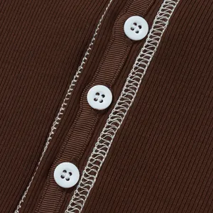 Primo piano di bottoni bianchi e cuciture a contrasto su maglia a coste marrone.