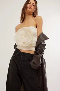Dettaglio di un top a fascia bianco senza spalline con un grande fiore 3D decorativo.