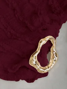 Dettaglio di una fibbia dorata irregolare su tessuto plissettato color bordeaux