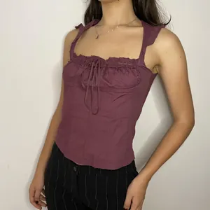 Dettaglio di una canotta in cotone viola con bordo in pizzo e dettaglio con fiocco