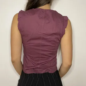 Vista posteriore di una blusa in cotone prugna senza maniche con balze sulle spalle.