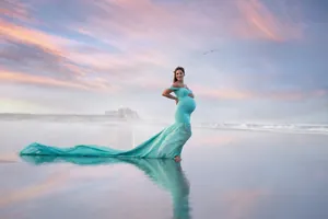 Elegant teal maternity photography gown with long flowing chiffon train on a beach