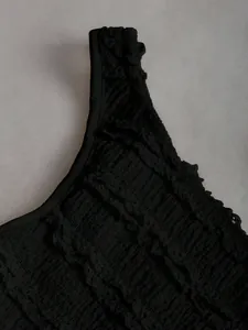 Dettaglio di un crop top nero con texture arricciata e bordi a volant di alta qualità.