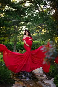 Elegant red off-shoulder maternity gown with long flowing chiffon train for photography.