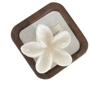 Large white frangipani flower hair claw clip with elegant marble effect on wooden tray.