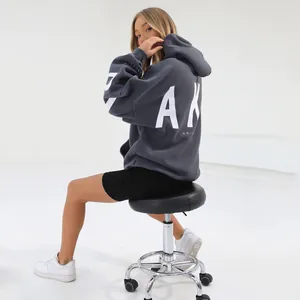 Oversized grey hoodie with large back print shown on a model sitting on a stool.