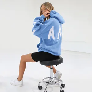 Detail view of a blue oversized hoodie with bold white back print on a model sitting