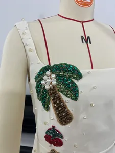Close-up of white dress featuring intricate beaded palm tree and pearl embellishments.