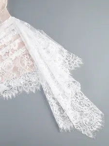 Detailed close-up of white floral lace fabric with delicate eyelash trim on a mesh dress