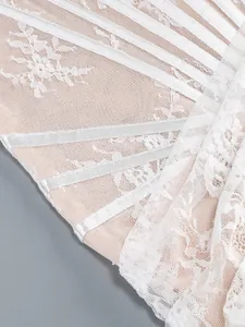 Detail view of intricate white floral lace and satin ribbon on sheer cocktail dress