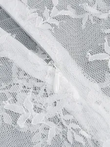 Close-up of white lace dress with concealed zipper detail and floral embroidery pattern.
