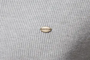 Primo piano dettagliato del tessuto del maglione in maglia grigia e del badge in metallo AIOPESON