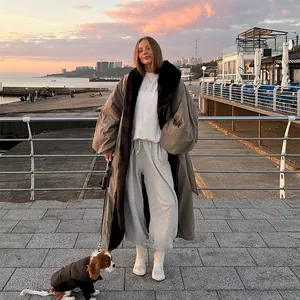 Elegant long khaki trench coat with black fur collar shown in a sunset outdoor setting