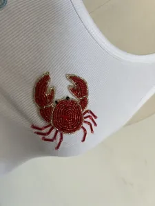Gros plan d'un débardeur blanc côtelé avec une décoration de crabe en perles rouges.