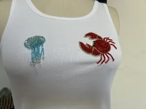 Gros plan d'un débardeur blanc côtelé avec broderie de méduse et homard en perles