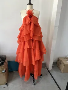 Detail view of an orange tiered ruffle halter dress with a 3D floral chest accent.