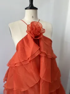 Close-up detail of a bright orange halter dress featuring 3D flower and layered ruffles