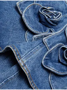 Detailed close-up view of intricate 3D denim flower applique and stitching on blue dress