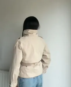 Back view of a khaki short trench coat with stand collar and waist belt details.