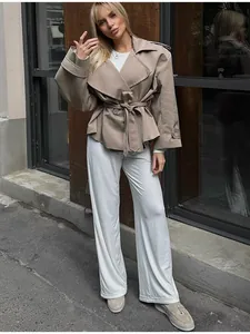 Model trägt einen kurzen khakifarbenen Trenchcoat mit Gürtel und weite weiße Hosen