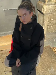 Lifestyle shot of a woman wearing a black double-breasted wool jacket with stand collar