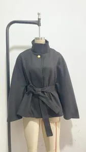 Detalle de una elegante chaqueta tipo capa negra con botón dorado y cinturón a juego.