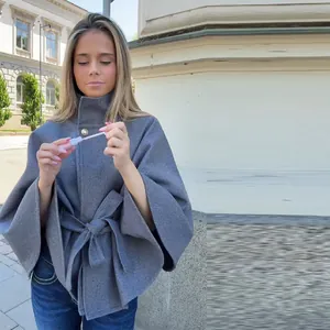 Primer plano de la textura de lana y la hebilla de metal de esta elegante chaqueta tipo capa.