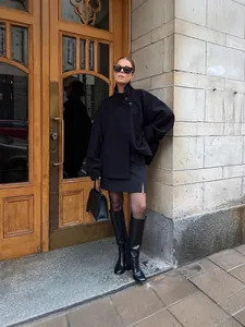 Chic black stand-collar wool coat with matching skirt and high boots in city street