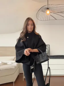 Elegante chaqueta tipo capa negra para mujer con hebilla metálica y cinturón a juego.