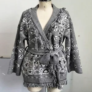 Détail du cardigan en maille grise de style ethnique avec franges et ceinture assortie.