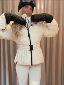 Schicke weiße Damen-Skijacke mit Taillengürtel und schwarzem Winterzubehör für die Piste.