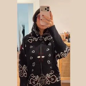 Close-up of a stylish black knit zip-up cardigan featuring intricate white and red paisley prints