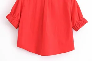 Détail d'une chemise rouge à manches courtes avec ourlet incurvé et manches bouffantes.
