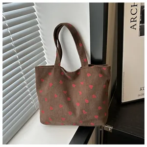 Close-up of brown corduroy tote bag with red strawberry pattern and shoulder straps