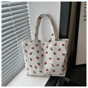 Detailed close-up view of the strawberry pattern on a soft white corduroy tote bag