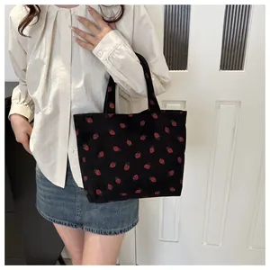 Close-up view of a black corduroy tote bag featuring cute red strawberry patterns in use