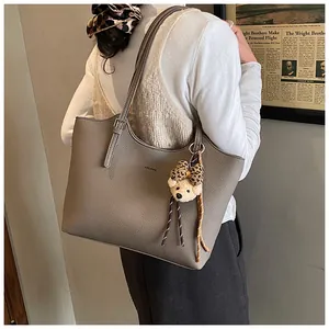 Detail view of a large taupe pebbled leather tote bag featuring a cute bear charm with bow