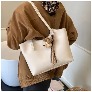 Detailed lifestyle view of a white pebbled leather tote bag featuring a cute bear charm