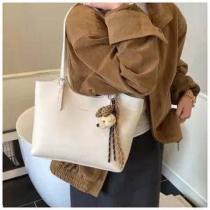 Close-up of a stylish white pebbled leather tote bag featuring a cute animal charm
