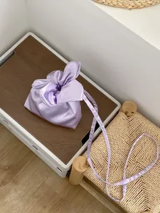 Detail shot of the purple satin drawstring crossbody bag placed on a tray next to a woven stool.