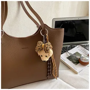 Detailed view of a brown vintage leather tote bag with a plush bear charm in office setting