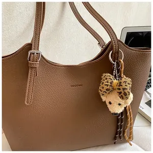 Detail view of a brown pebbled leather tote bag featuring a leopard print bow bear charm