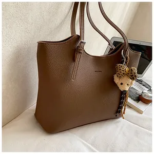 Detailed view of a vintage brown pebbled leather tote bag featuring a cute bear keychain