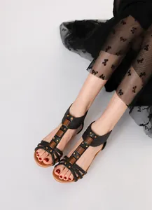 Elegantes sandalias romanas negras con cuña y tachuelas doradas en una modelo.
