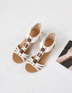 Primer plano de sandalias de cuña blancas con bloques de madera y tachuelas doradas.