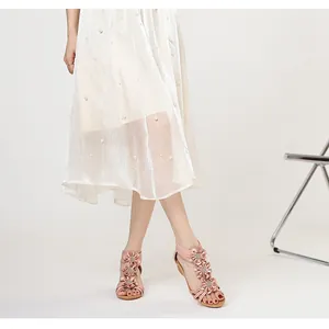 Lower body detail view of pink floral Bohemian sandals paired with a white pearl skirt.